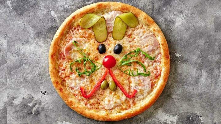 En pizza med ett kaninansikte av grönsaker.