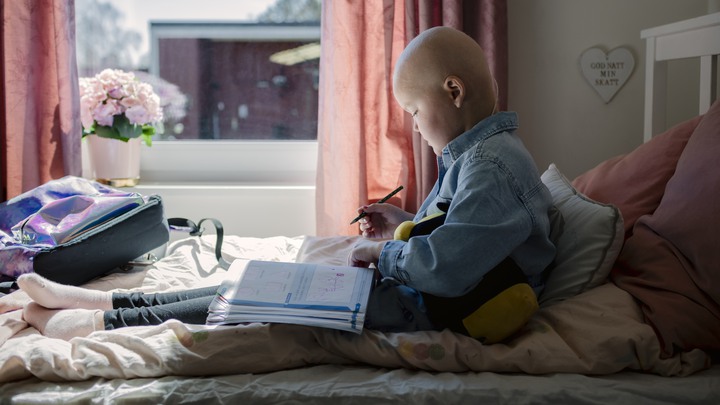 Alice sitter i sin säng med en skolbok och penna i knät
