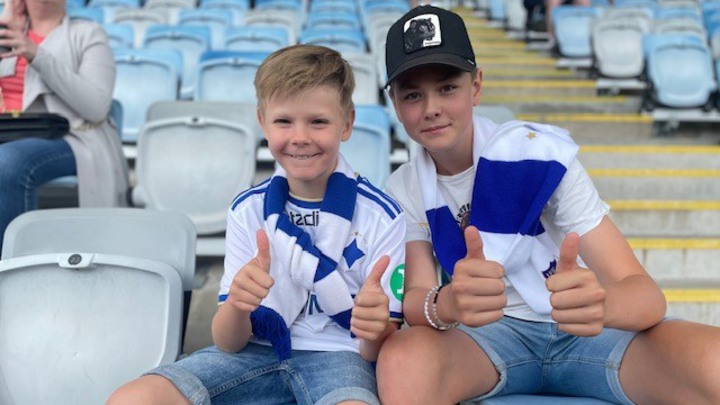 Tim och Vilgot sitter på läktaren vid en fotbollsmatch.