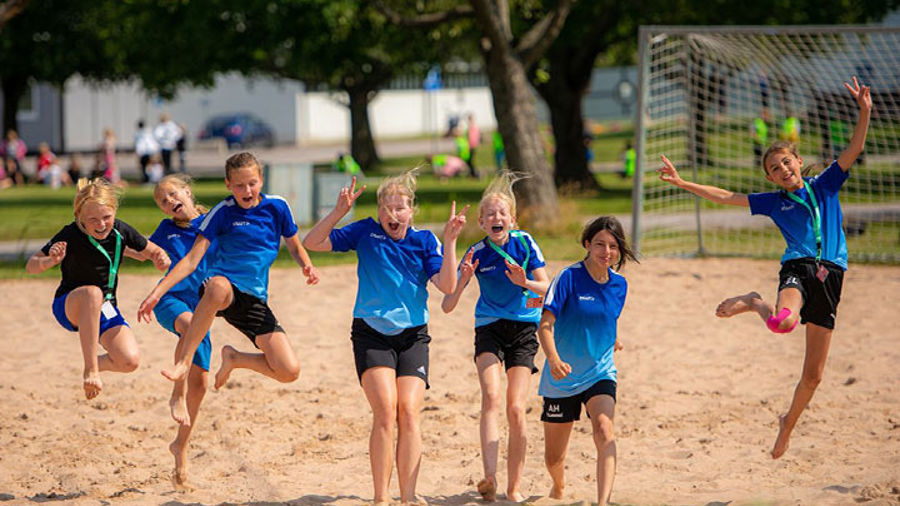 Barn i sportkl&auml;der som hoppar i sand.