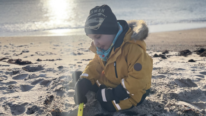 Caspian sitter på stranden, med jacka, vantar och mössa och gräver