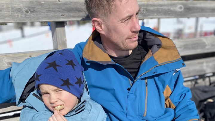 Karl och Joakim sitter ute på en bänk en solig vinterdag. Karl äter chips.