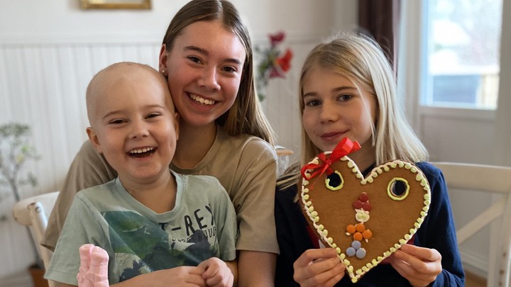 Karl sitter i sin syster Elsas knä, med Signe bredvid. Signe håller i ett stort pepparkakshjärta.