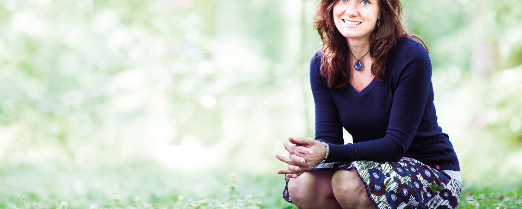 Camilla ler och sitter på huk i en skogsdunge.