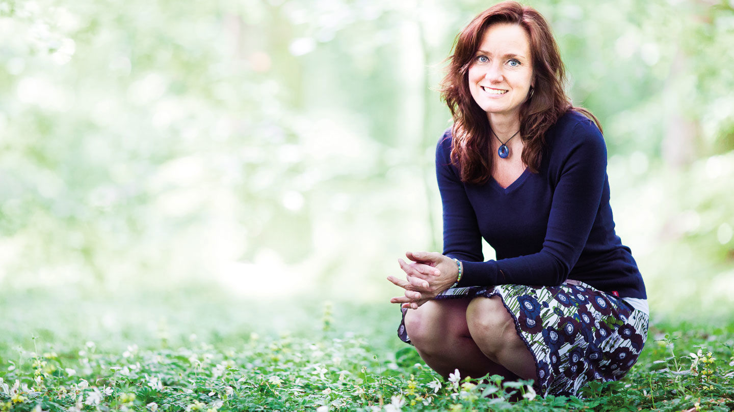 Camilla ler och sitter på huk i en skogsdunge.