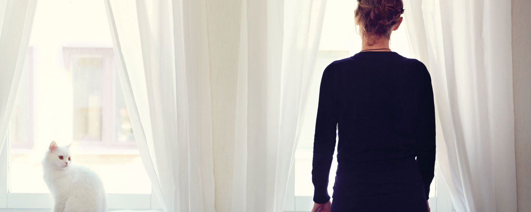 Caterina ser ut genom ett fönster. Hennes katt sitter bredvid.