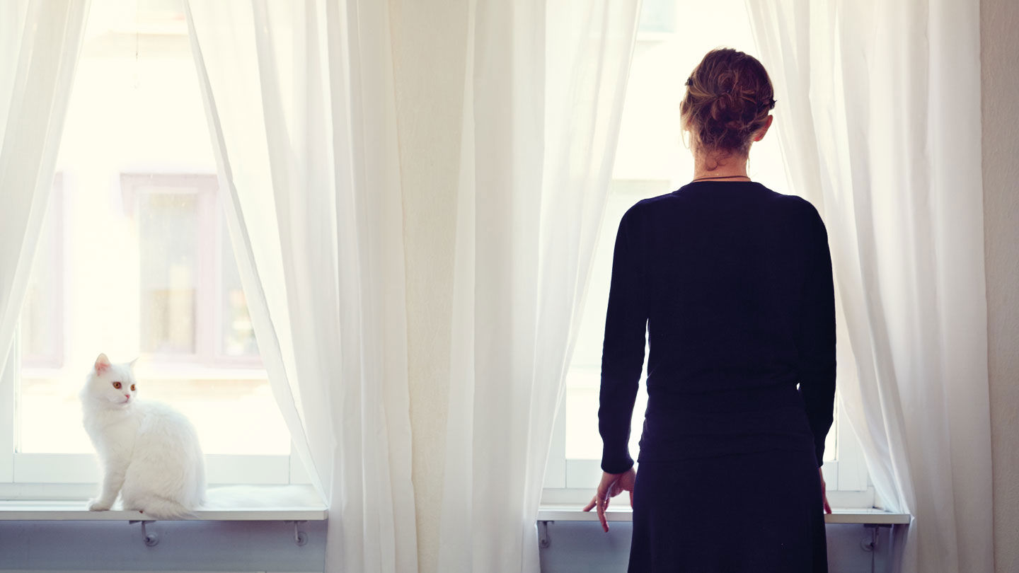 Caterina ser ut genom ett fönster. Hennes katt sitter bredvid.