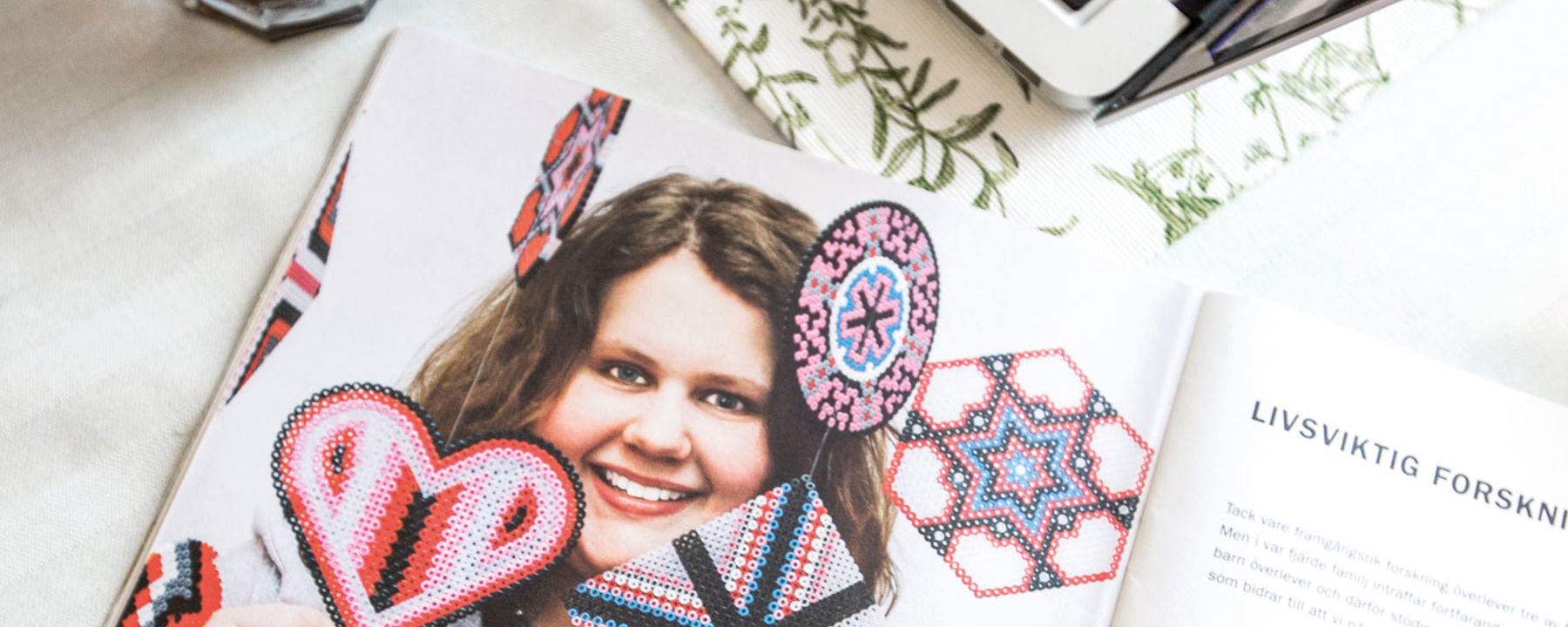 En tidsskrift ligger öppen på ett bord. Ellinor med sina pärlplattskreationer är med på bilden tryckt i uppslaget.
