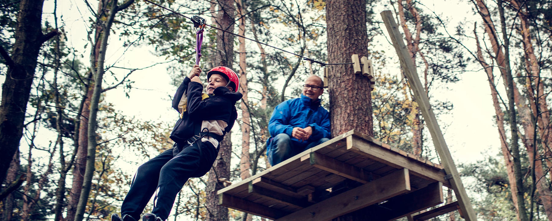 Ett barn åker linbana medan en vuxen tittar på.