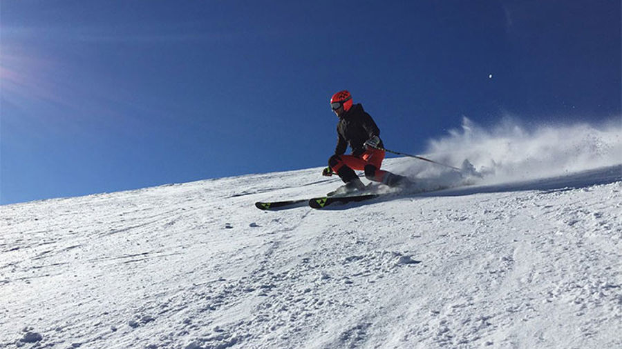 Ensam skidåkare i backe med blå himmel och solsken