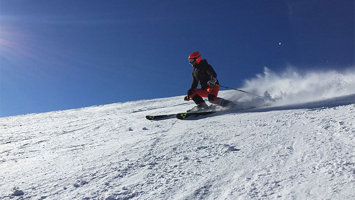 Ensam skidåkare i backe med blå himmel och solsken