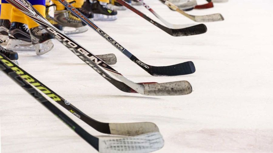 Fötter med hockeyrör och en lång rad hockeyklubbor på isen