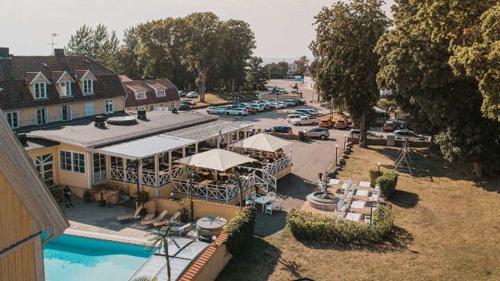 Drönarbild över hotellbyggnad med veranda, uteplatser och pool. Sommarbild.