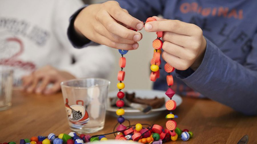 Två händer håller i snöre med färgglada pärlor, SuperSnöret