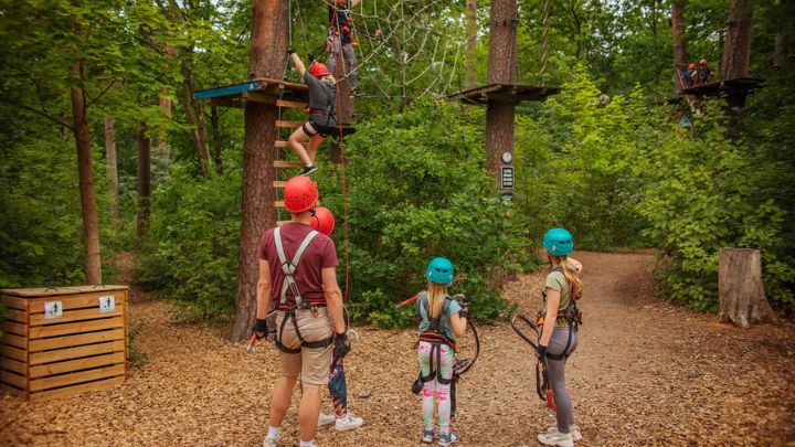 En vuxen och två barn tittar på en som klättrar i start på höghöjdsbana.