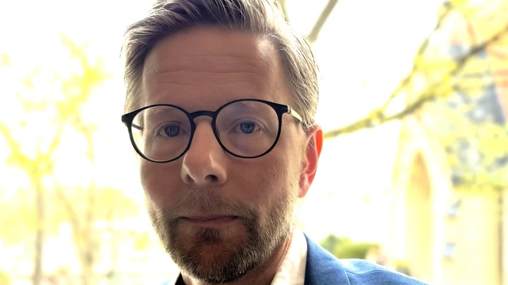 En man med skägg och glasögon tittar in i kameran.