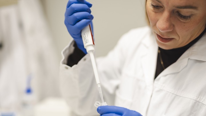 En kvinna i labbrock och blå handskar håller i ett rör